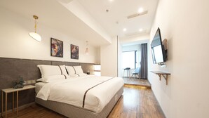 Ein modernes Schlafzimmer mit einem großen Bett, Nachttischen, einem an der Wand montierten Fernseher und Blick in den angrenzenden Raum.