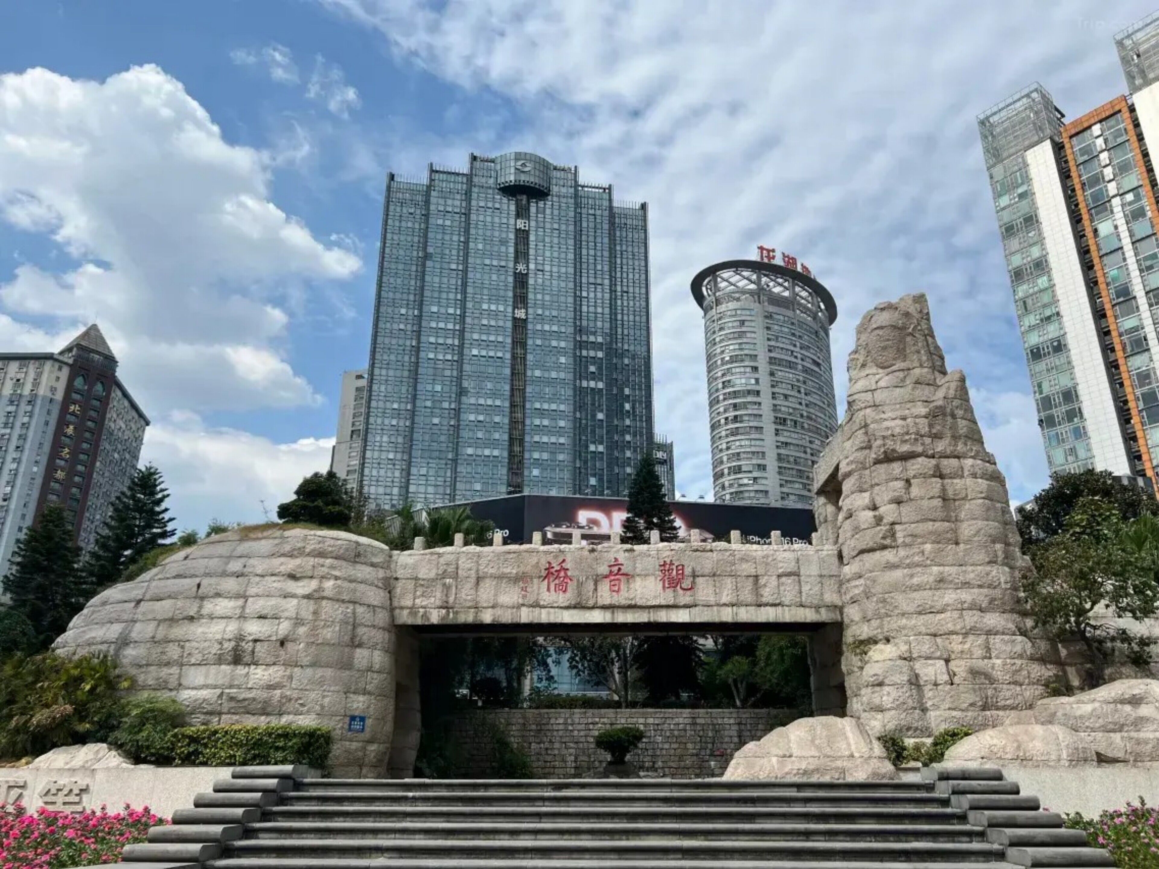A modern building with a glass facade, surrounded by stone structures and greenery.