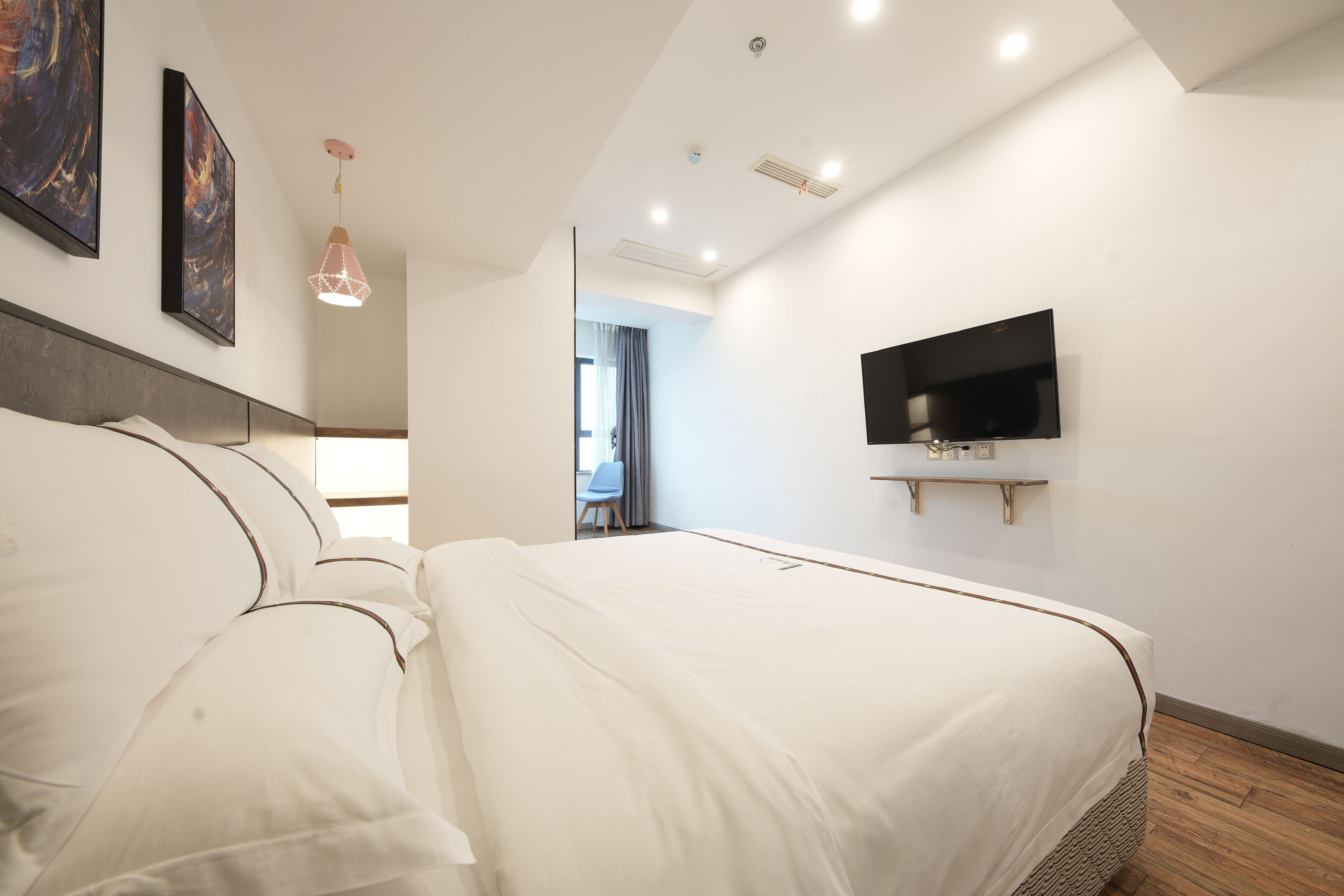 Un dormitorio moderno con una cama grande, un televisor de pantalla plana montado en la pared y una lámpara en el techo.