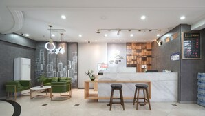 Ein modernes Hotel-Foyer mit einer Marmor-Apotheke, grünen Sofas und einem Stadtbild-Mural.