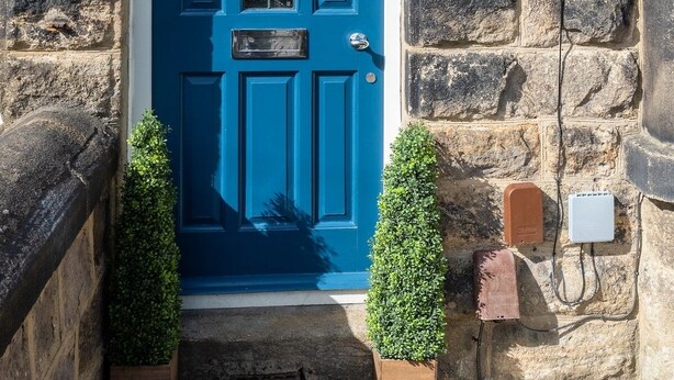 A blue door with the number 51, a small window with a decorative grille, and a stone wall with a security camera and electrical boxes. - Beautiful Townhouse Harrogate, 3 bedroom (Harrogate)