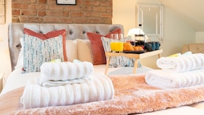 A hotel room with a brick wall, a bed with white and striped towels, a breakfast tray with croissants and orange juice, and a wooden side table. - Beautiful Townhouse Harrogate, 3 bedroom (Harrogate)