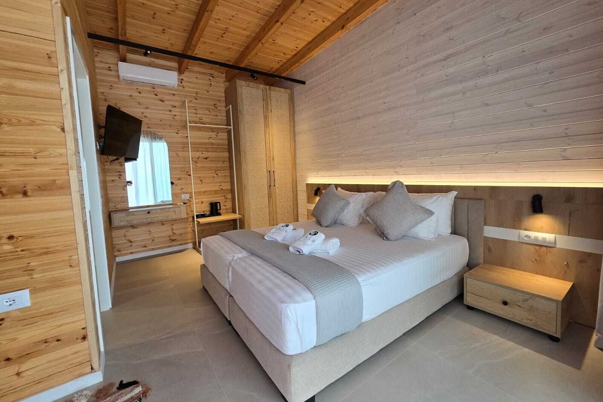 Un dormitorio moderno con techo y paredes de madera, una cama grande con almohadas, una mesita de noche y un televisor montado en la pared.