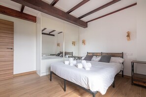 A bedroom with a bed, wooden beams, a mirror, and a small table.