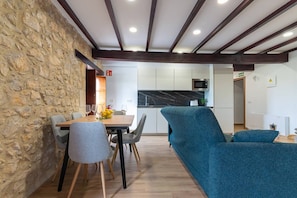A dining area with a stone wall, wooden beams, and a modern kitchen in the background. - InfinityCoast V byFidalsa (Piélagos)