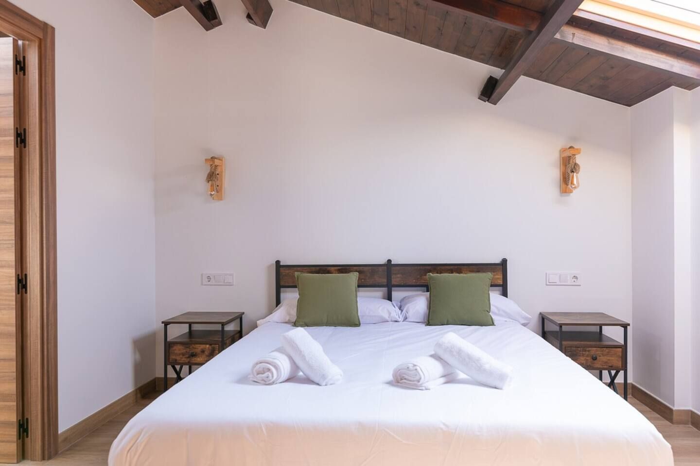 Un dormitorio con una cama grande, dos mesitas de noche y techo de madera.