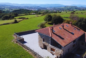 A stone building with a red-tiled roof, surrounded by green fields and distant mountains. - InfinityCoast V byFidalsa (Piélagos)