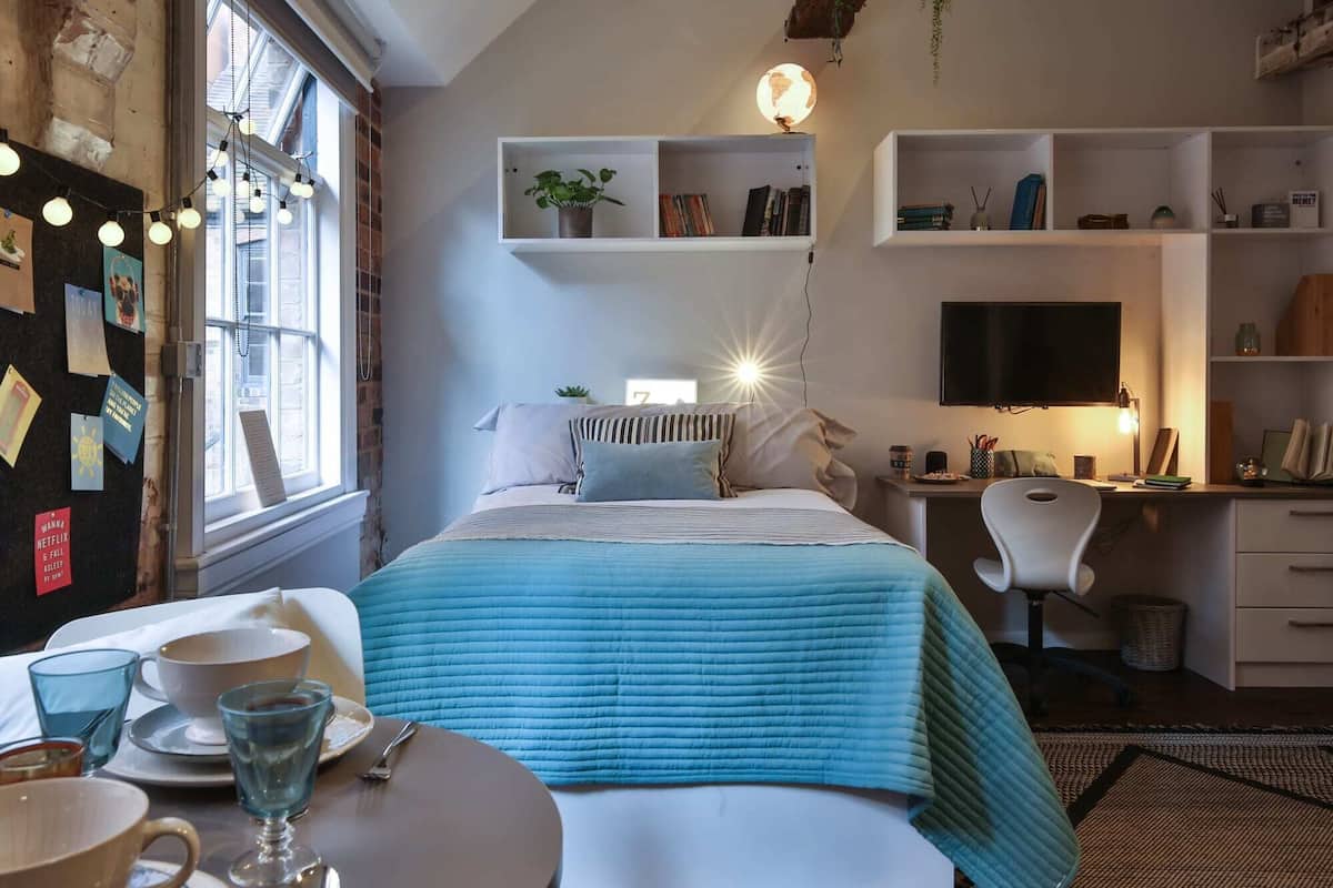 Un dormitorio con cama, mesita de noche y zona de escritorio con silla.