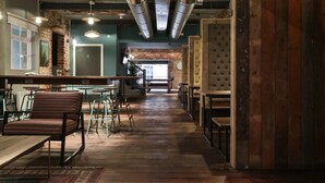 Un restaurant avec un plancher en bois, des chaises vertes et des tables. On y trouve des luminaires suspendus et un mur en briques.