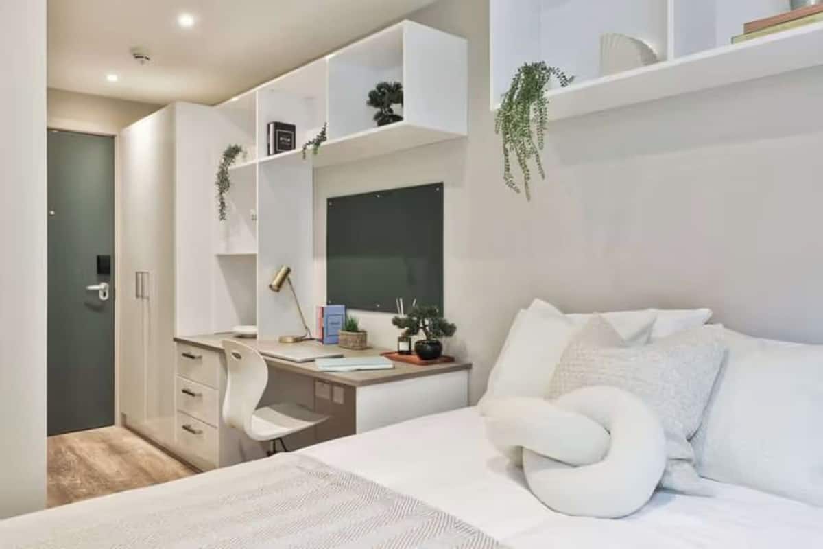 Un dormitorio moderno con una cama grande, un escritorio con silla y estanterías empotradas con plantas.