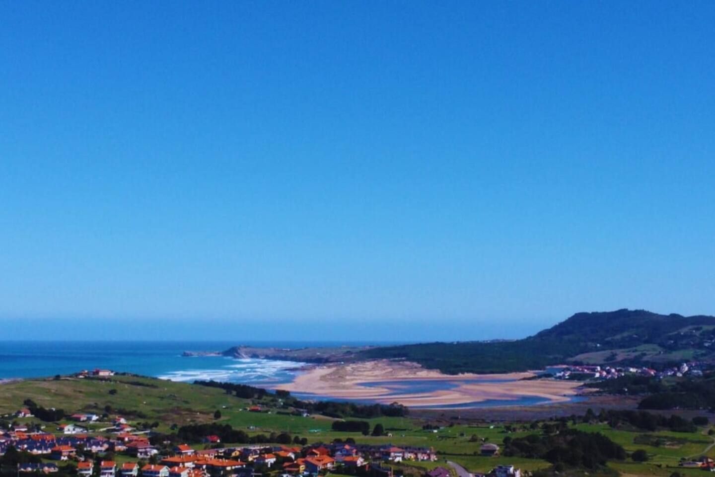 Une ville côtière avec des maisons, une plage et des collines en arrière-plan.