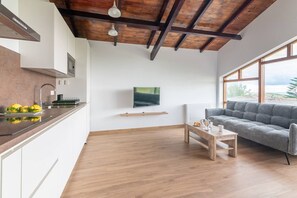 Eine moderne Küche mit Holzbalkendecke, einem Wand-Fernseher und einem grauen Sofa in einem Wohnbereich mit Holzboden.