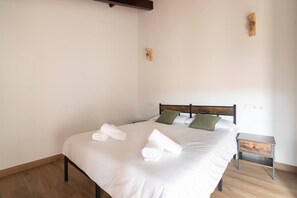 Ein ordentlich bezogenes Bett mit weißen Leinentüchern und aufgerollten Handtüchern, ein hölzerner Kopfteil und ein kleiner Nachttisch mit Schublade.