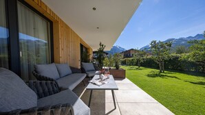 Un espacio moderno al aire libre con sofás y una mesa, con vistas a un césped cuidado y montañas a lo lejos.