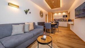 Una sala moderna con un sofá gris, una mesa redonda de centro y un comedor con techo de madera.
