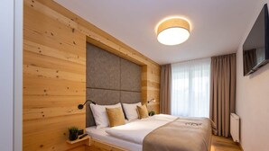 A modern bedroom with a wooden headboard, a bed with white linens, a bedside table with a plant, and a mounted TV.