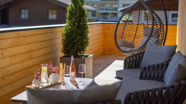 A balcony with a hanging chair, a sofa, and a table set with glasses and a bottle.