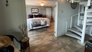 A bedroom with a bed, a nightstand, a lamp, and a staircase.