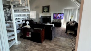 A spacious loft with a high ceiling, a built-in staircase, a fireplace, a television, and a cozy seating area.