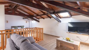A modern loft with exposed wooden beams, a large TV, and a cozy seating area with a sofa and a dining table. - Infinity Coast V by Fidalsa (Miengo)