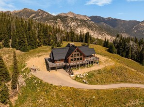 Een lodge met een ruim terras, omgeven door bergen en dicht bos.