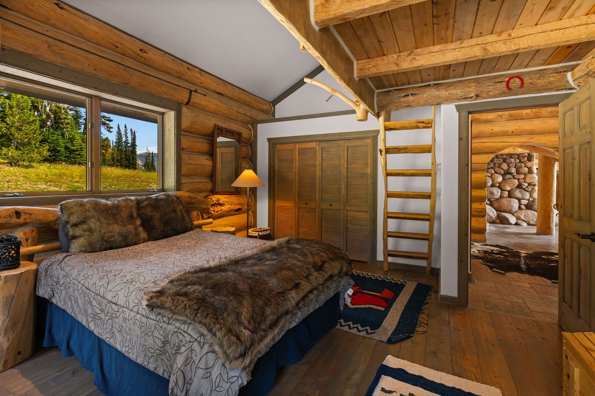 Een slaapkamer in een blokhut met een groot bed, een houten ladder en een stenen muur.