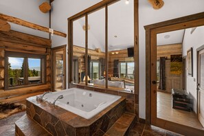 Een badkamer in chaletstijl met een ruim bad, houten balken en uitzicht op de natuur.