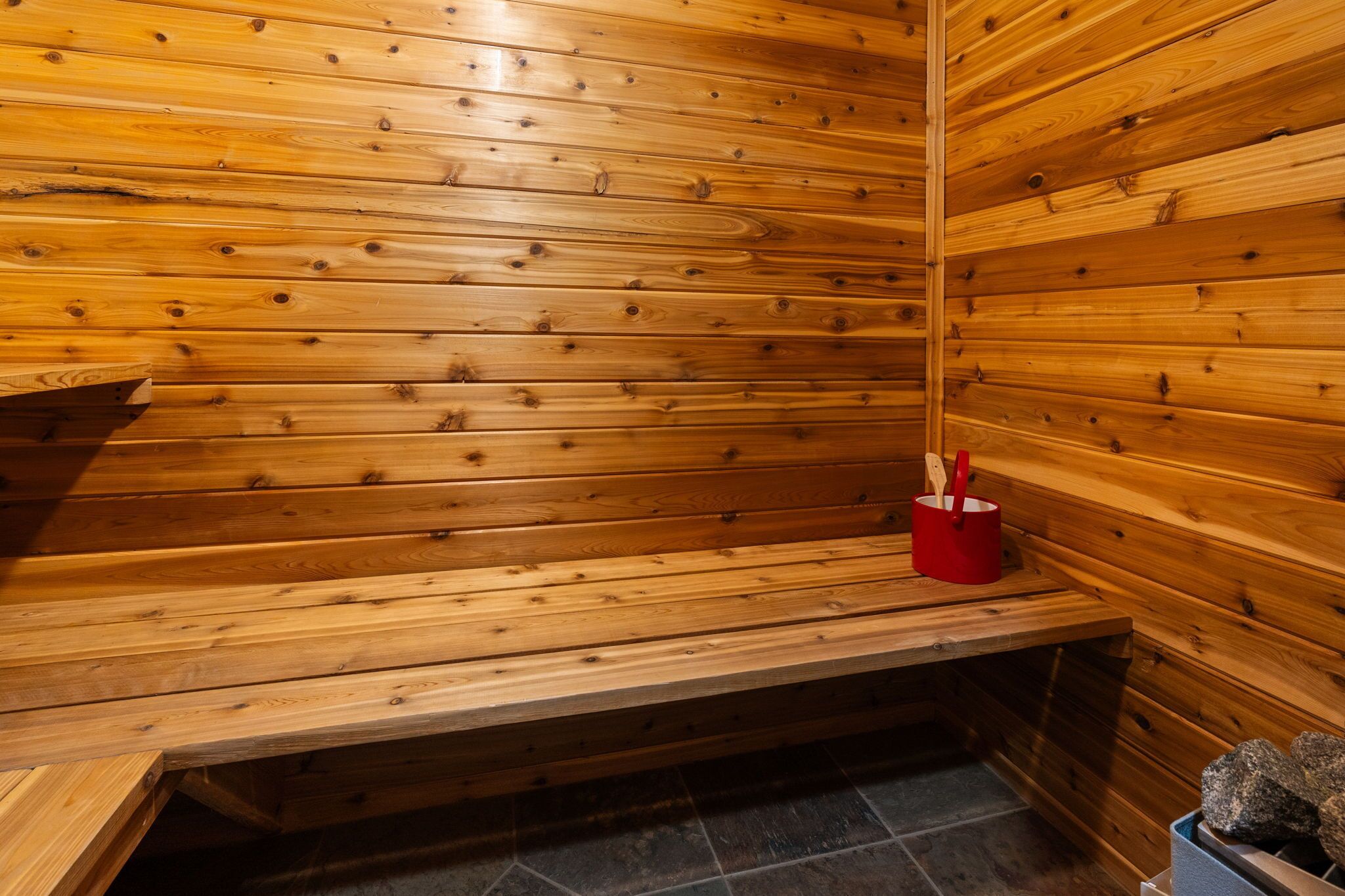 Een houten sauna met banken en een rode container voor accessoires.