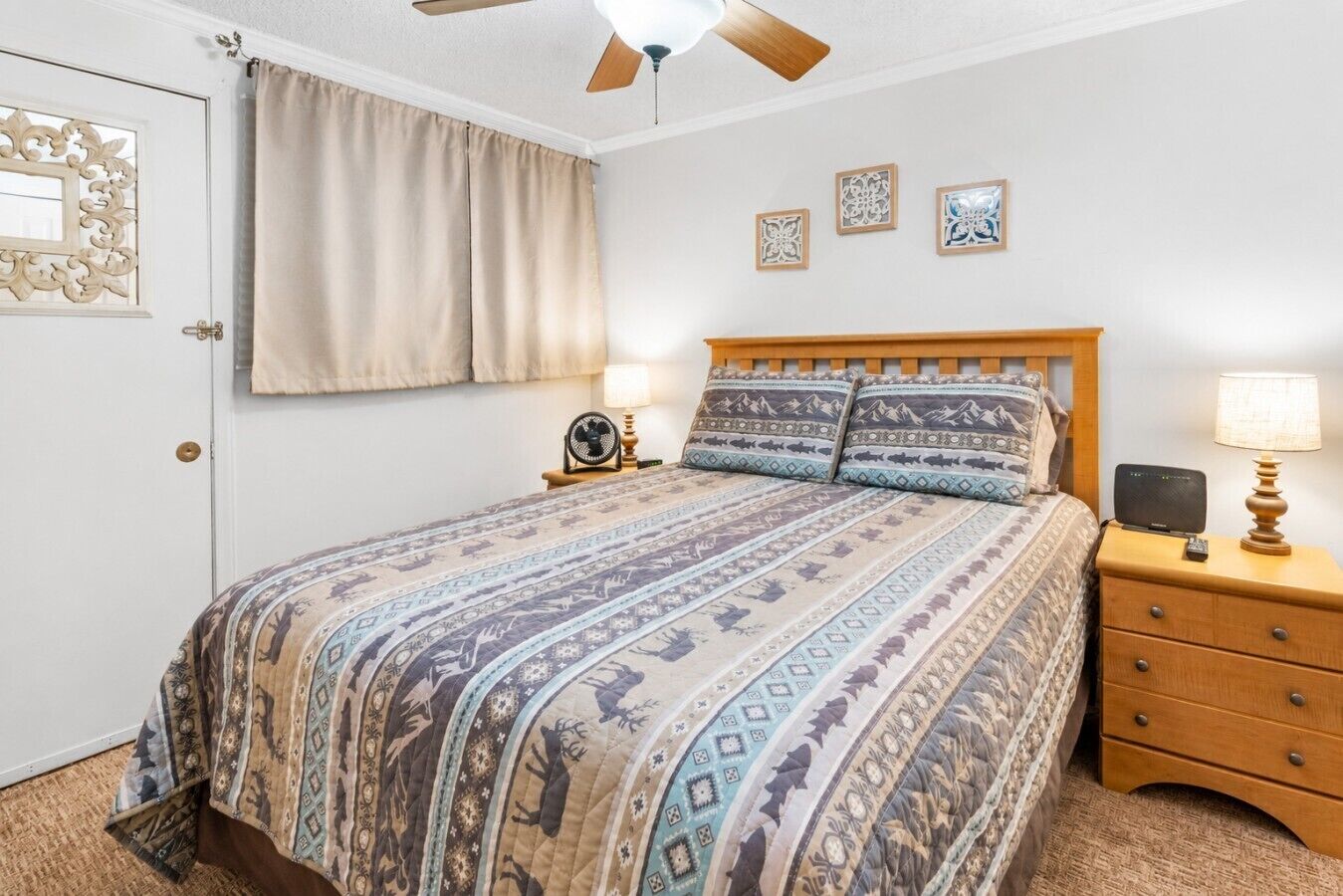 Een slaapkamer met een bed, nachtkastjes, een plafondventilator en decoratieve muurkunst.