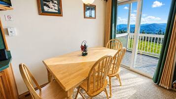 Zona pranzo con tavolo e sedie in legno, una lampada a sospensione e vista su un balcone con ringhiera.
