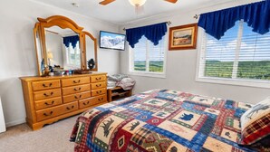 A bedroom with a wooden dresser, a bed with a quilt, a ceiling fan, and a window with a view of a green landscape. - ML178 Great Views & Location EZ Parking  Next To Village (Snowshoe)