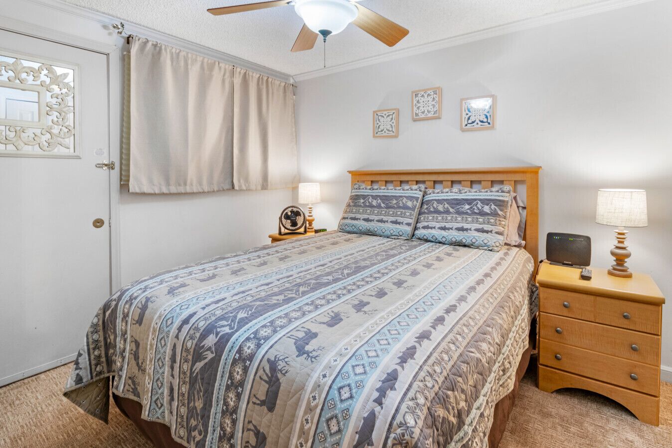 A bedroom with a bed, nightstands, a ceiling fan, and wall art.