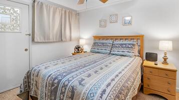 A bedroom with a bed, nightstands, a ceiling fan, and wall art.