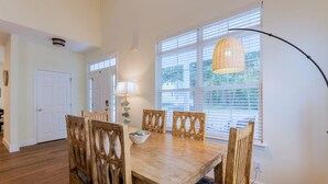 Un coin repas avec une table et des chaises en bois, une lampe et une fenêtre avec des stores.