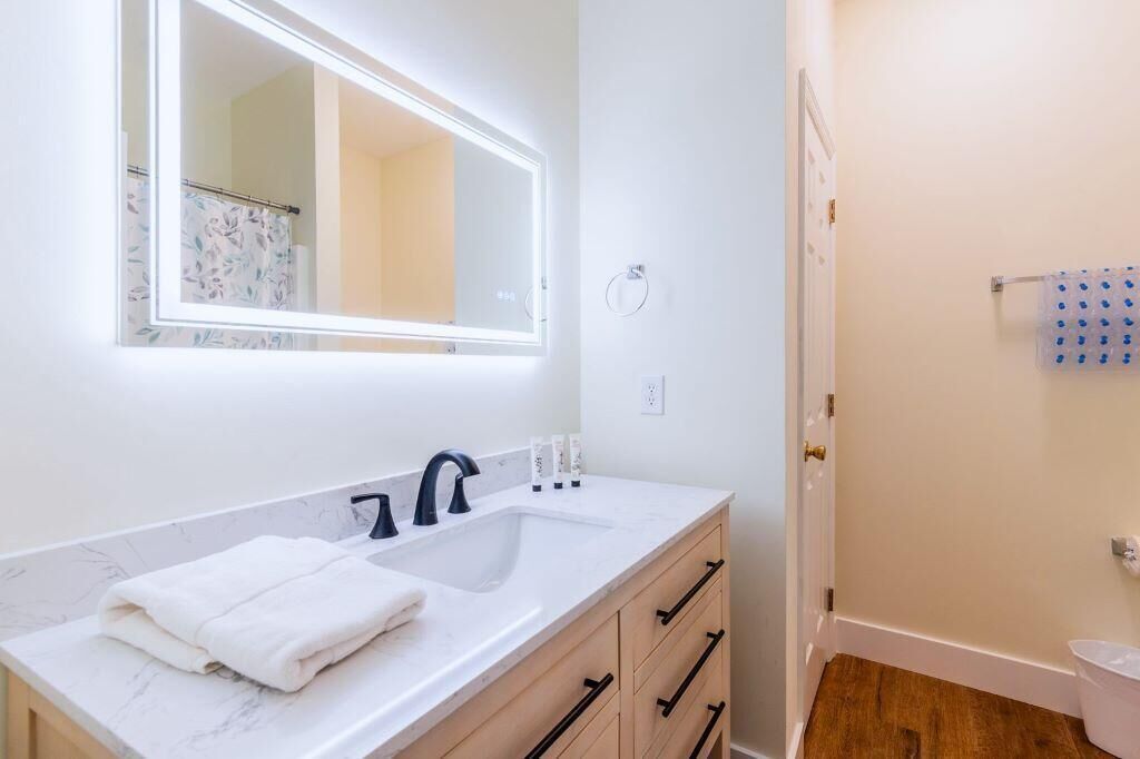A bathroom with a white vanity, a large mirror, a sink, and a shower area.