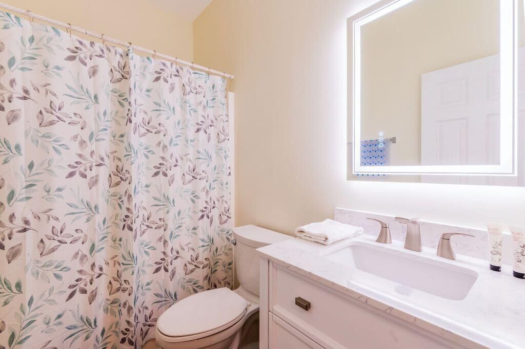 A bathroom with a floral shower curtain, a toilet, a sink with a mirror, and toiletries on the counter.