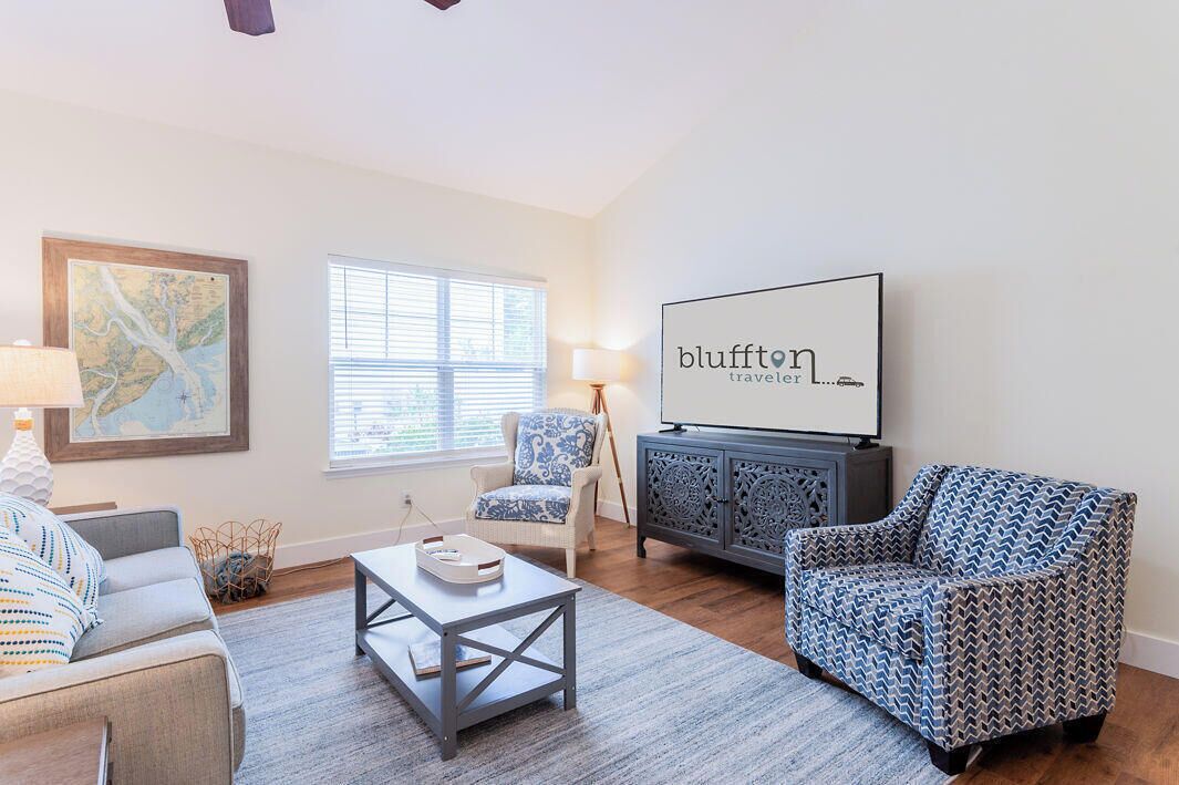 A living room with a sofa, armchair, coffee table, and a flat-screen TV mounted on the wall.