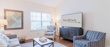 A living room with a sofa, armchair, coffee table, and a flat-screen TV mounted on the wall.