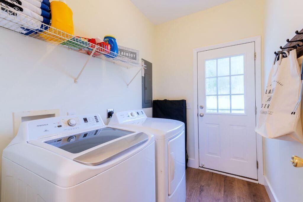 Un espace buanderie comprenant un lave-linge et un sèche-linge à chargement frontal, une étagère avec des produits de lessive et une porte avec une fenêtre.