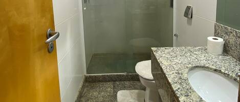 Un baño moderno con ducha de vidrio, inodoro blanco, encimera de granito y espejo.