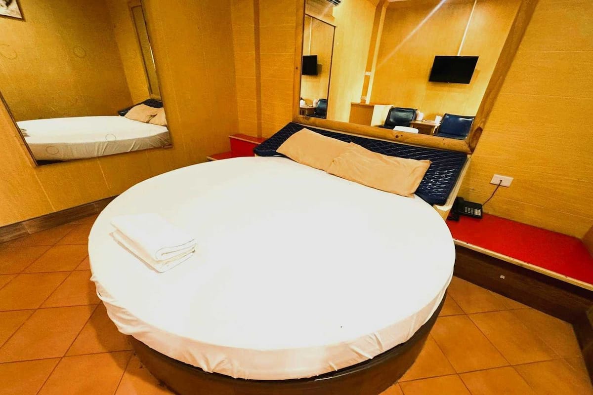 Una habitación de hotel con una cama redonda, un pequeño rincón de descanso, un televisor y un espejo.