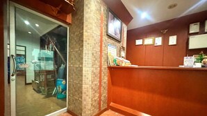 Zona de recepción con puerta de vidrio que da a una habitación, mostrador de recepción de madera y suelo de baldosas.