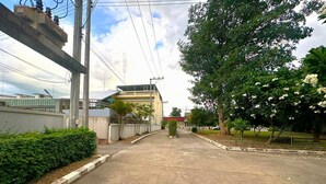 Una calle tranquila con un edificio de techo plano y línea de techo roja. Hay árboles y un seto a lo largo de la acera.
