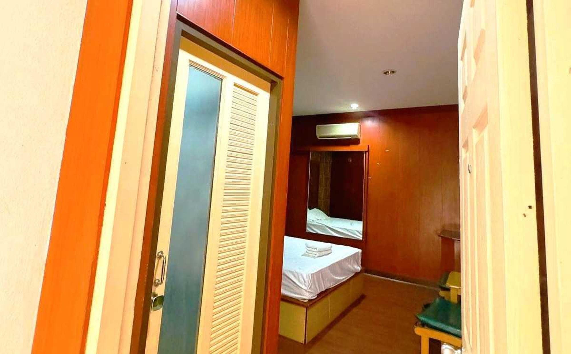 A narrow hallway leading to a room with a bed, a small table, and a window.