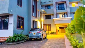 A modern multi-story residential building with a car parked in the driveway. - Entebbe Serenity breeze apartments - Single Room with Lake View (Entebbe)