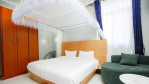 A bedroom with a bed, a green sofa, a small round table, and a wardrobe. - Entebbe Serenity breeze apartments - Single Room with Lake View (Entebbe)