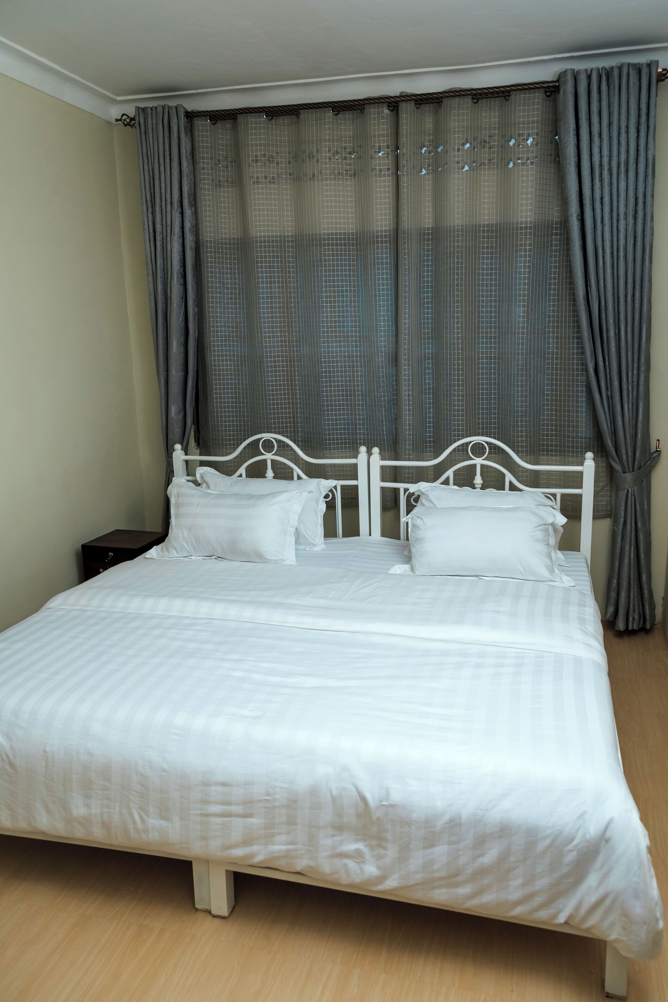 Una cama bien tendida con ropa blanca y almohadas, un cabecero de metal blanco y una mesita de noche de madera a su lado.