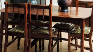 A dining table with six wooden chairs, a vase with flowers, and a black refrigerator in the background. - Kandez Holiday Home (Entebbe)
