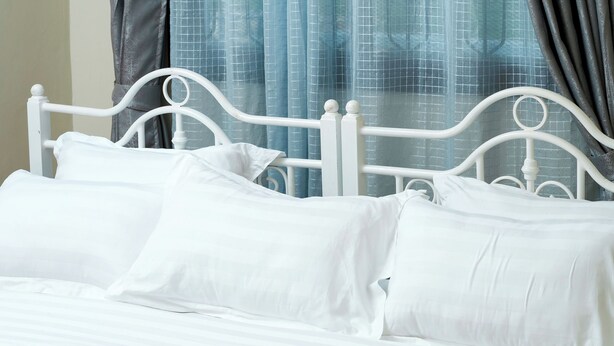 A bed with white bedding and a metal frame, curtains, and a window with a view. - Kandez Holiday Home (Entebbe)