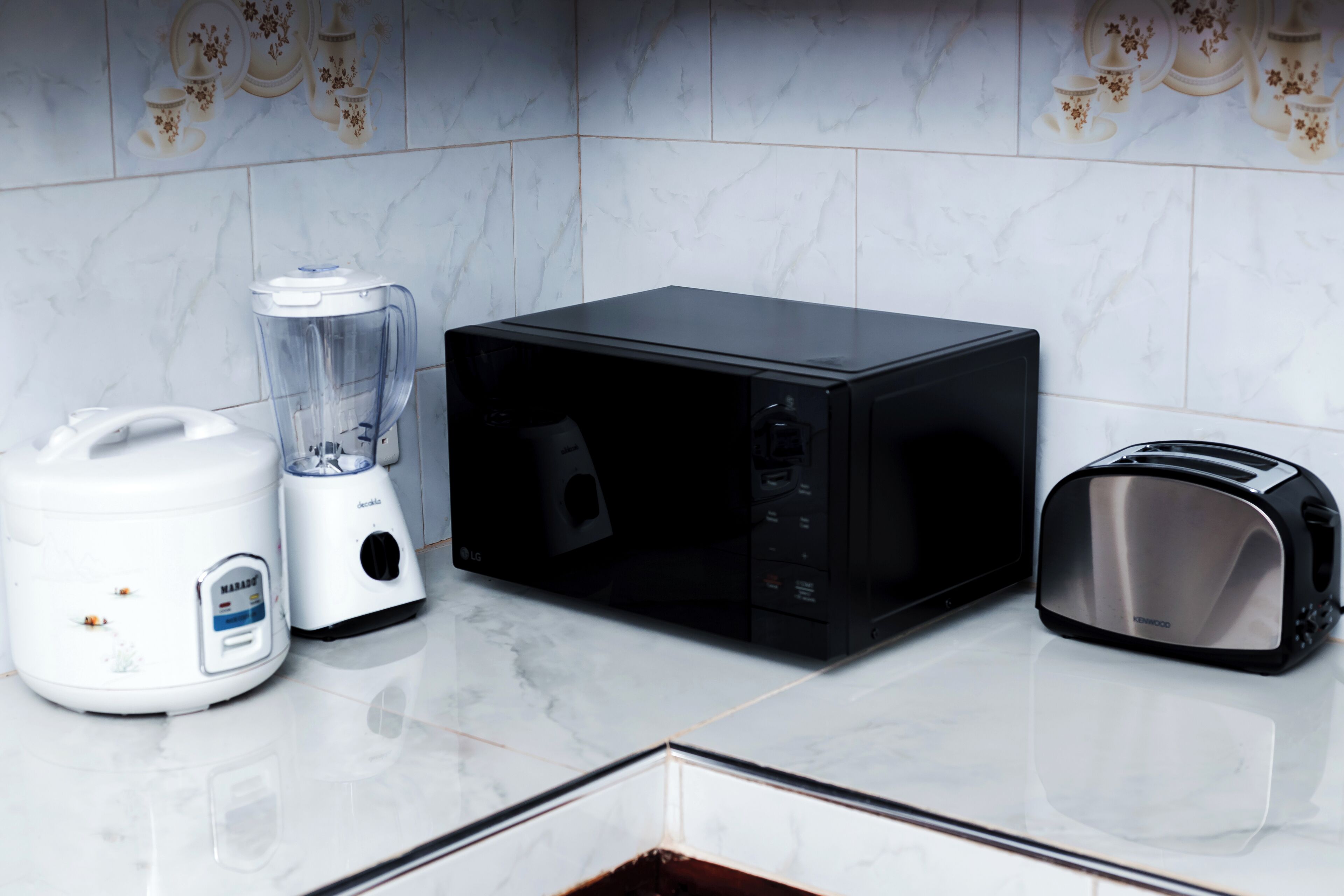 A kitchen with a blender, microwave, and toaster on a marble countertop.